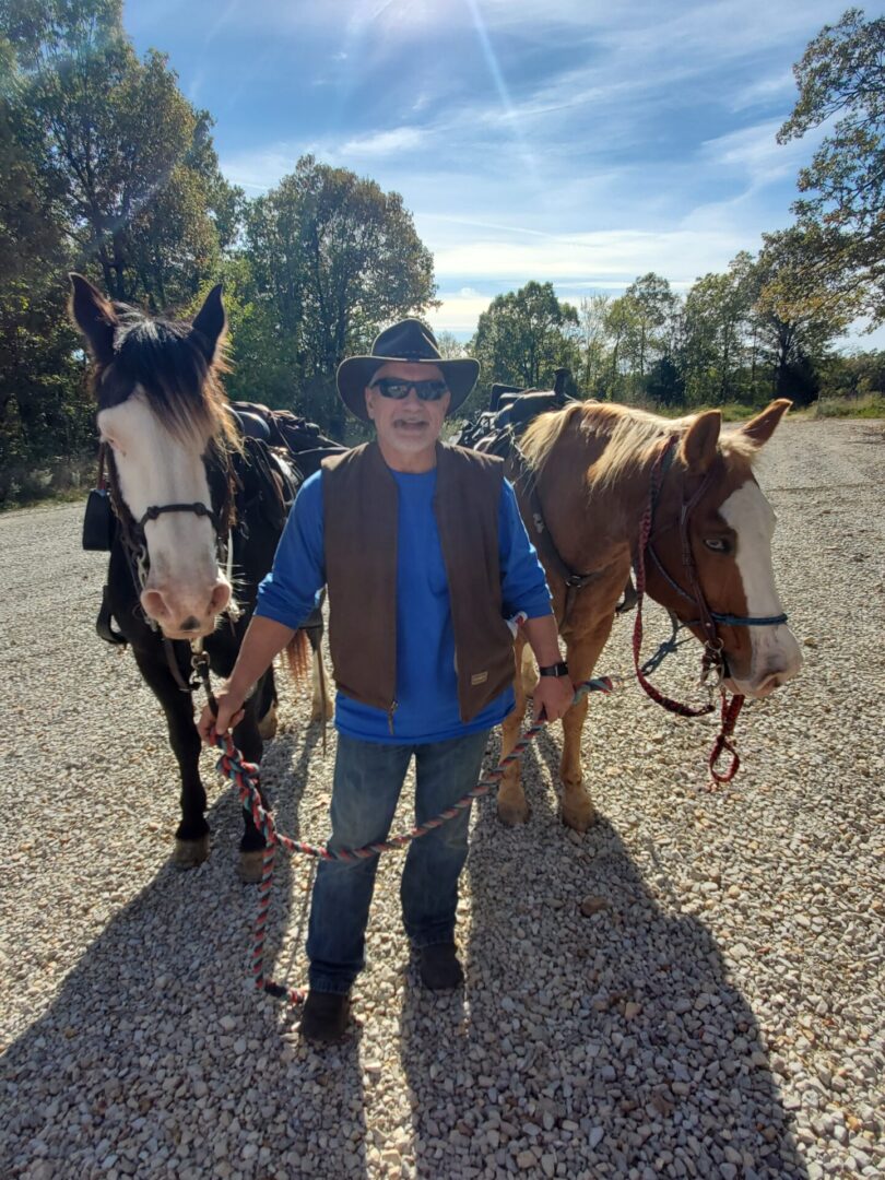 A man standing next to two horses on gravel.